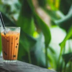 Overhead view of orange Thai iced tea with milk swirls, star anise, cinnamon, and cardamom pods.