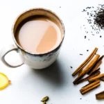 A steaming mug of masala chai with cinnamon sticks and cardamom pods on wood.