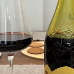 An old bottle of 1979 Chateauneuf du Pape wine next to a glass decanter on wood.