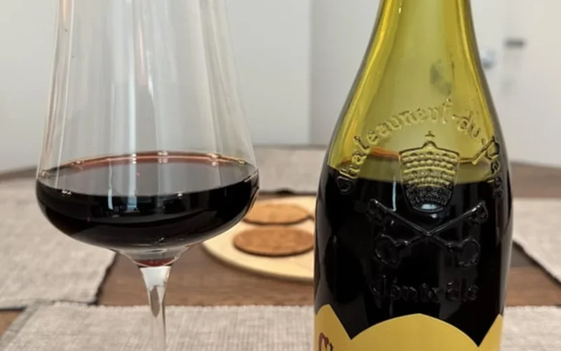 An old bottle of 1979 Chateauneuf du Pape wine next to a glass decanter on wood.