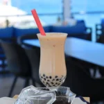 A pink kitten miniature teapot emitting dry ice smoke next to a boba milk tea.