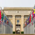 Wide shot of an empty international diplomatic assembly hall with rows of desks and microphones.