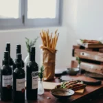 A red wine bottle and a white wine bottle resting on a dark wooden table.