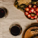 Overhead view of red wine in glasses next to a cheese and fruit platter.