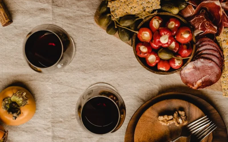 Overhead view of red wine in glasses next to a cheese and fruit platter.